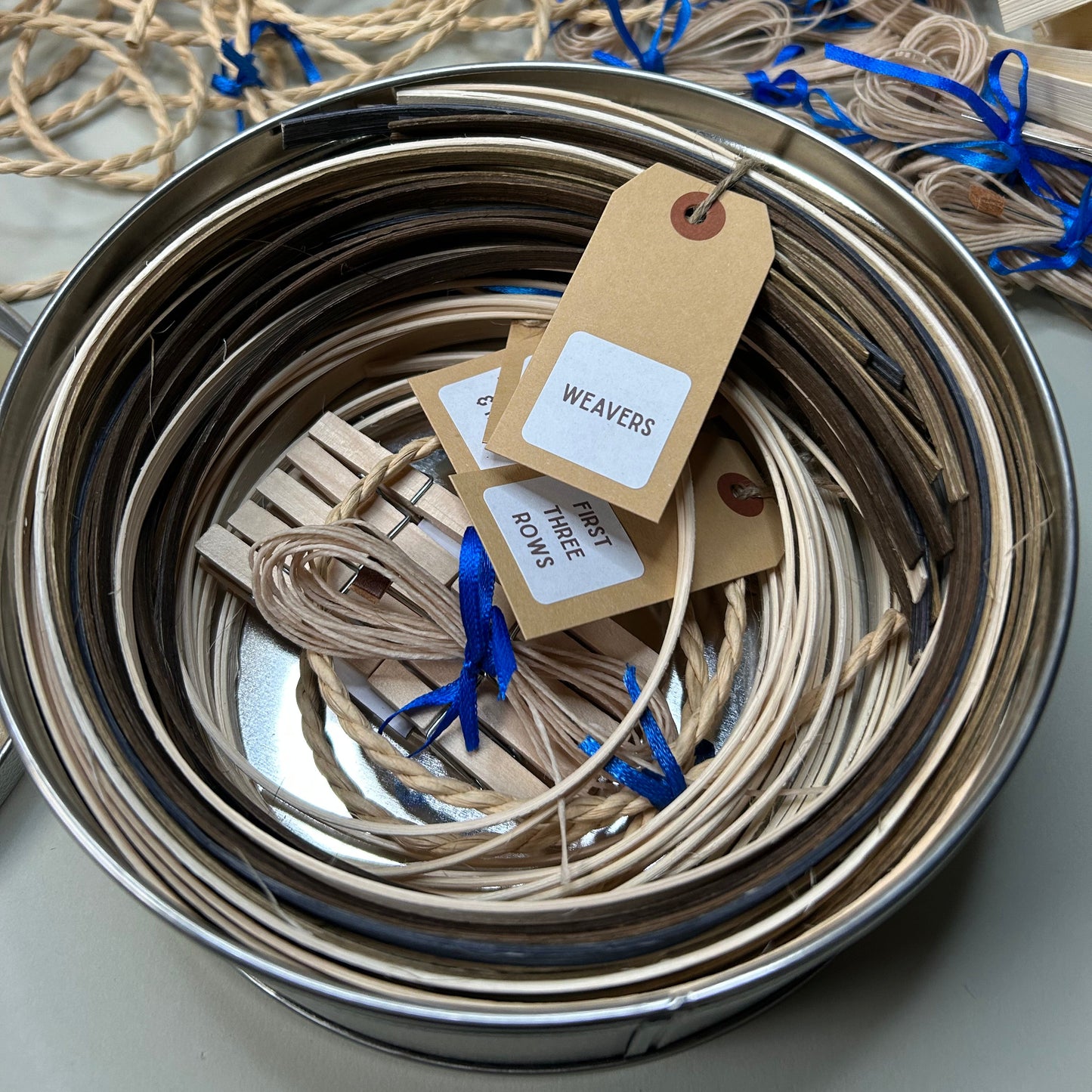 Metallic spools of thread with tags inside a metal container, surrounded by additional thread spools.