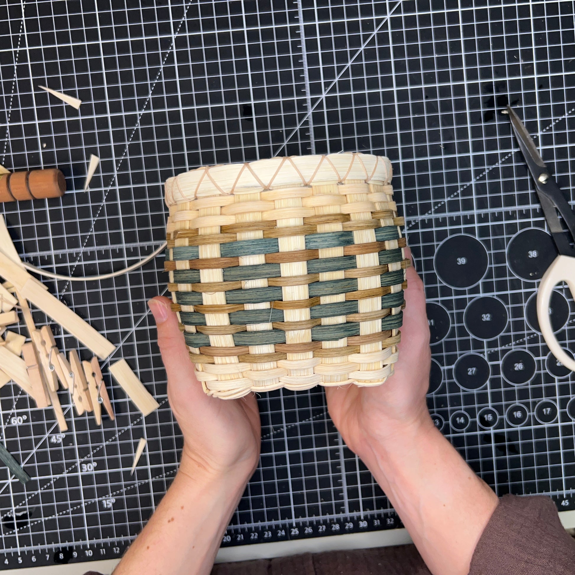 Handmade woven basket held by a person on a cutting mat with tools.