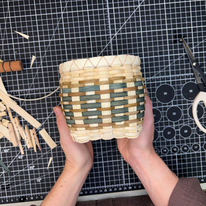 Handmade woven basket held by a person on a cutting mat with tools.