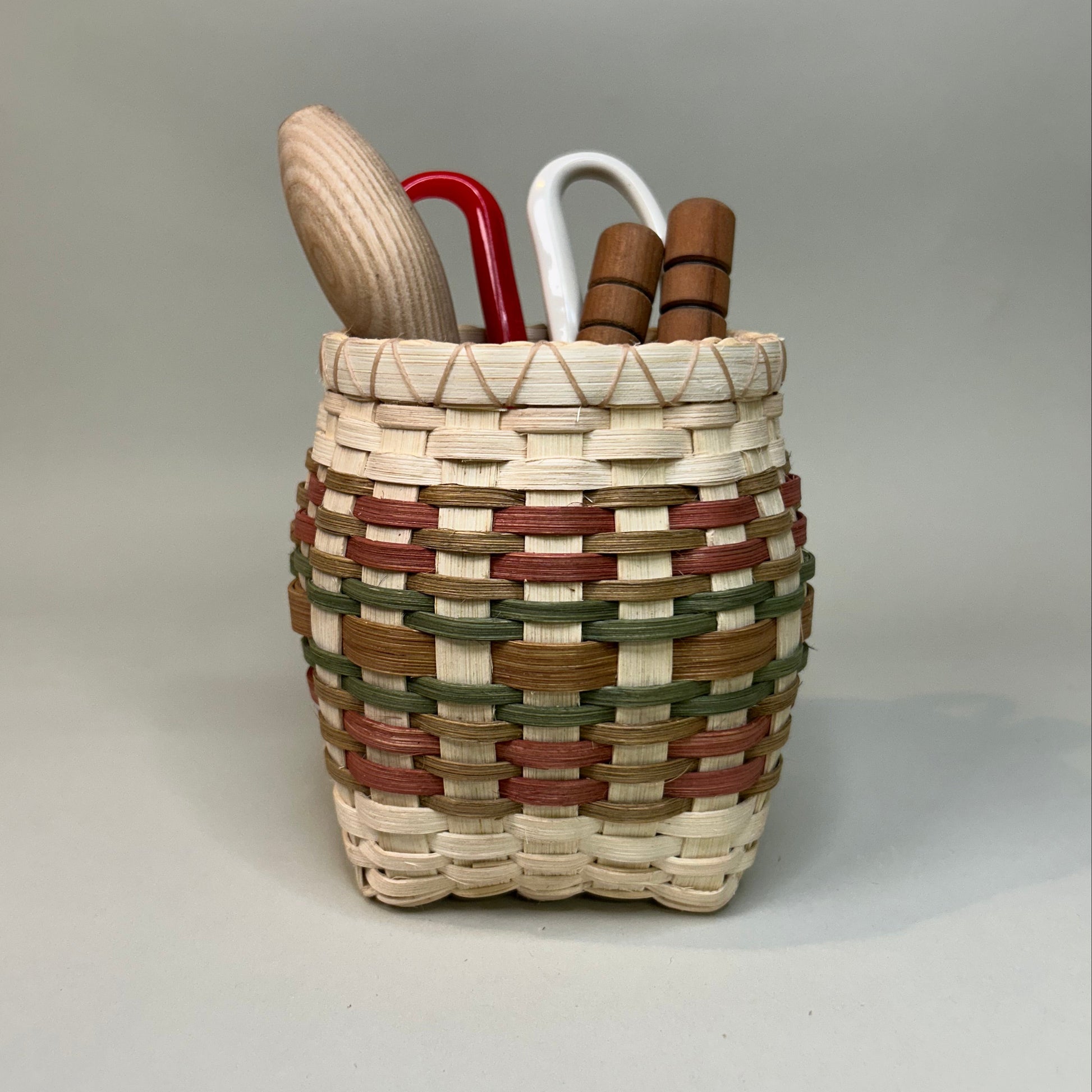 Woven basket with wooden handle and red tool on a light gray background